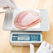 A gloved hand weighing sliced ham on an Edlund digital portion scale.
