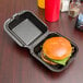 A hamburger in a Genpak black foam takeout container.