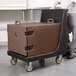 A man pushing a brown Cambro tray and sheet pan carrier on a black cart.