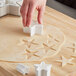 A person's hand using an Ateco plastic star cutter to cut out star shaped cookies.