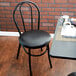 A Lancaster Table & Seating black hairpin chair with black vinyl seat sits at a table with a white cup of coffee.