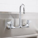 A stainless steel Equip by T&S wall mount faucet with gooseneck spout and lever handles over a sink.