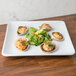 An American Metalcraft white square stoneware platter with clams, salad, and greens on a table.