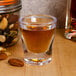 A close up of a GET SAN plastic shot glass with brown liquid and nuts.