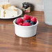 A white Fiesta ramekin filled with raspberries and blueberries on a white table.