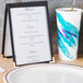 A black Menu Solutions table tent displaying a menu on a table in a fine dining restaurant.