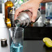 A person using a Vollrath stainless steel cobbler cocktail shaker to pour a drink.
