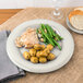 A Carlisle Sierrus melamine plate with chicken, potatoes and green beans, a plate of bread, and a glass of wine.