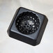 A black plastic square floor sink strainer with holes in it.