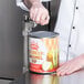 A person using a Choice Prep Light Duty Manual Can Opener to open a can of caramel dip on a table in a professional kitchen.