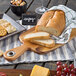 A Tablecraft acacia wood display bread board with sliced bread, crackers, and cheese.
