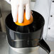 A gloved hand squeezes an orange into a juicer.