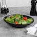 A Libbey Driftstone Onyx satin matte porcelain coupe bowl filled with spinach salad on a table.