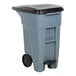 A grey Rubbermaid commercial trash can with black lid.