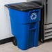 A blue Rubbermaid recycling bin with a white recycling symbol on it.