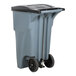 A grey plastic Rubbermaid trash can with black wheels.