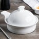 A white porcelain Libbey casserole dish with a handle and lid on a wooden surface.