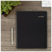 A black At-A-Glance monthly business planner on a wood surface with a pen.