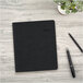 A black rectangular At-A-Glance Daily Action Planner with text on the cover and a pen on a white surface.