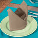 A folded beige Intedge cloth napkin on a plate with a fork.