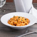 A white Elite Global Solutions melamine bowl of pasta with sauce and herbs and a fork.