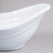 A close-up of a white Elite Global Solutions oblong melamine sauce dish with a curved shape.