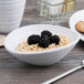 A white Elite Global Solutions swirl oblong melamine bowl filled with oatmeal and blackberries with a spoon inside.