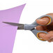 A person using Westcott titanium bonded scissors with gray and yellow handles to cut a purple sheet of paper.