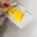 A person slicing a yellow bell pepper on a WebstaurantStore flexible cutting board.
