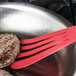 A red Mercer Culinary slotted spatula flipping meat patties in a pan.