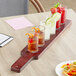 An Acopa mahogany flight paddle with straight up tasting glasses holding a variety of drinks on a wooden board.