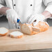 A person in white gloves using a Mercer Culinary Millennia Colors blue bread knife to cut bread on a cutting board.