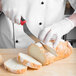 A person in white gloves using a Mercer Culinary Millennia Colors® red bread knife to slice bread.