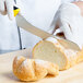 A person in white gloves using a Mercer Culinary yellow bread knife to slice a loaf of bread.