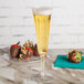 A WNA Comet clear plastic champagne flute filled with champagne on a table with chocolate covered strawberries.