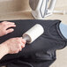 A hand using a 3M Scotch-Brite lint roller to remove lint from black fabric.