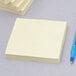 A stack of 3M Canary Yellow Post-It Super Sticky Note pads with a blue pen on a gray surface.