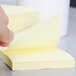 A hand holding a 3M Canary Yellow Super Sticky Note pad.