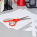 A pair of 3M Scotch multi-purpose scissors with a red handle cutting paper.