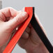 A person holding a red and black piece of 3M Scotch Outdoor Mounting Tape.