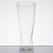 A WNA Comet clear plastic pilsner glass on a white surface with a small amount of liquid in it.