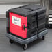 A black Metro Mightylite front loading food pan carrier with a red door on a cart.