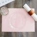 A Hoffmaster pink paper placemat with a scalloped edge on a table with a glass.