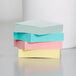 A stack of 3M Post-It notes in assorted pastel colors on a white surface.