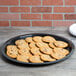 A Fineline black plastic catering tray holding a plate of cookies on a wood surface.