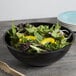 A bowl of salad with yellow peppers in a black plastic catering bowl.