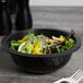 A bowl of salad with yellow pepper and lettuce in a black Fineline low profile plastic bowl.