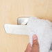 A person using a Bobrick double robe hook to hang a white fluffy towel.