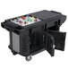 A black Cambro Versa Ultra work table with heavy-duty casters holding a large black cooler full of bottles.