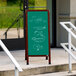 A cherry A-Frame sign board with a green chalkboard on a table with a price list written in chalk.